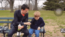 a man in a suit sits on a park bench next to a little boy who is crying and holding a bottle of champagne