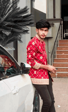 a man in a red shirt leans against a car