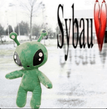 a stuffed green alien stands in front of a sylvain logo