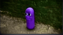 a purple cartoon character with big eyes is standing on a dirt road .