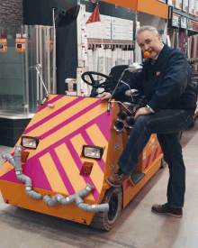 a man wearing a clown nose is sitting on a yellow and pink vehicle that says ' lg ' on it