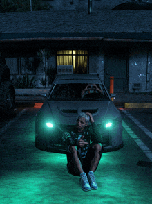 a man sits on the ground in front of a car that has green lights on it