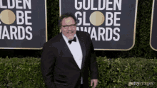 a man in a tuxedo and bow tie is standing in front of a sign that says golden globe awards