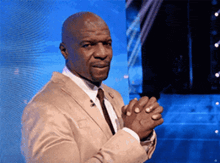 a man in a tan suit and tie holds his hands together