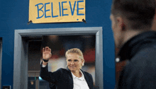 a woman stands in front of a sign that says believe on it