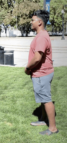 a man wearing a red shirt and grey shorts is standing in the grass