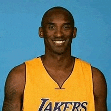 a man in a yellow lakers jersey is smiling for the camera .