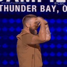 a man with a beard is standing in front of a microphone in front of a sign that says thunder bay on it .