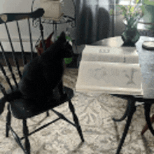 a black cat is sitting on a chair next to a table with a book open on it .