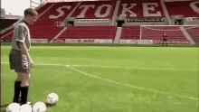 a man is standing on a soccer field in front of a stadium with a sign that says stoke .