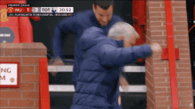 a man in a blue jacket is walking down a set of stairs with a premier league scoreboard behind him