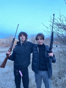 two young men standing next to each other holding shotguns