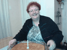 a woman in a black sweater sits at a table with a cake and a candle