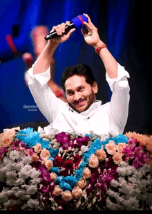 a man in a white shirt is holding a microphone in front of a display of flowers