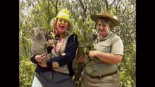 a woman in a hard hat is holding a koala bear while another woman holds a baby koala bear .