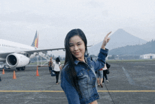 a woman in a denim jacket stands in front of an airplane