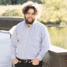 a man with curly hair and a beard is standing on a wooden bridge .