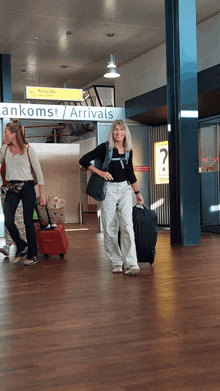 two women carrying luggage in front of a sign that says ankomst / arrivals