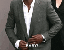 a man in a suit is adjusting his jacket while a woman stands behind him and says baby .