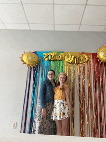 two girls are standing in front of a rainbow backdrop with the word dad written in gold