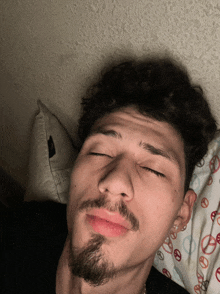 a man with his eyes closed is laying on a bed with a peace sign pillow