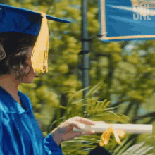 a woman in a graduation cap and gown holds a diploma in front of a sign that says she did