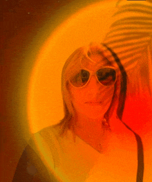 a woman wearing sunglasses stands in front of a yellow and red background