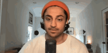 a man wearing an orange beanie and a white shirt is talking into a microphone