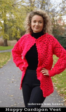 a woman wearing a pink crocheted cardigan vest stands on a path