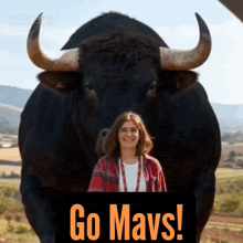 a woman stands in front of a very large bull that says go mavs on it