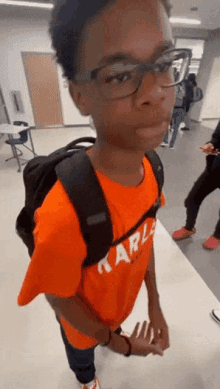 a boy wearing glasses and an orange shirt that says karls on it