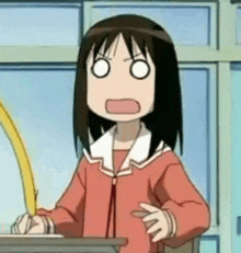 a girl is sitting at a desk with a pen in her hand making a funny face .