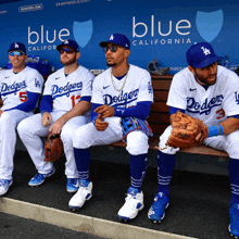 a group of dodgers players sit on a bench in a dugout