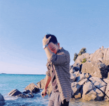 a man covering his face with his hand while standing on a rocky beach