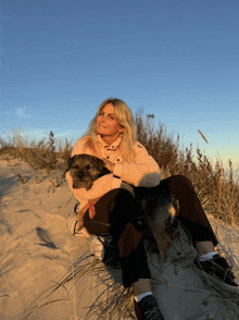 a woman sitting on a sand dune with a dog