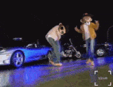 two cartoon characters are dancing in front of a blue car and motorcycle