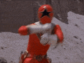 a red power ranger with a black star on his helmet is standing in the snow in the desert .