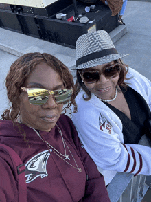 two women wearing hats and sunglasses are sitting next to each other and one of them is wearing a shirt that says tigers