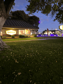 the outside of a denny 's restaurant with a tree in front of it