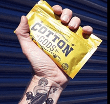 a man with a tattoo on his wrist is holding a bag of cotton pads .