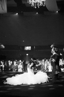 a black and white photo of a bride and groom dancing in front of a crowd