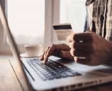 a man is holding a credit card while typing on a laptop .