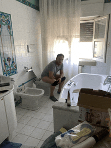 a man sits on a toilet in a bathroom with a box that says elli on it