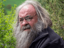 a man with long hair and a beard wears glasses and a black jacket