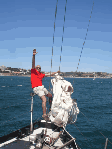 a man in a red shirt is sitting on a sailboat