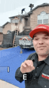 a man wearing a red hat and a shirt that says texas family roofing is standing in front of a house .