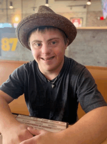 a young man wearing a hat sits at a table with a menu in front of him that says 87