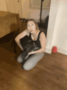 a woman in a black tank top is kneeling on the floor with a dog