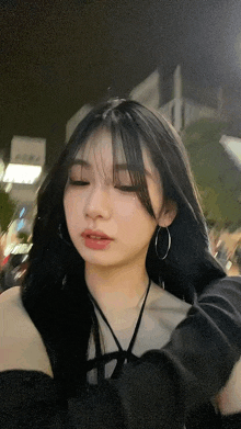 a woman with long black hair and hoop earrings is taking a picture of herself at night .