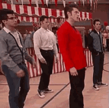 a group of young men are standing on a basketball court . one of the men is wearing a red shirt .